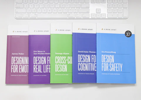 Designing for Emotion, Design for Real Life, Cross-Cultural Design, Design for Cognitive Bias, and Design for Safety paperbacks fanned out on a white desk below a white keyboard.