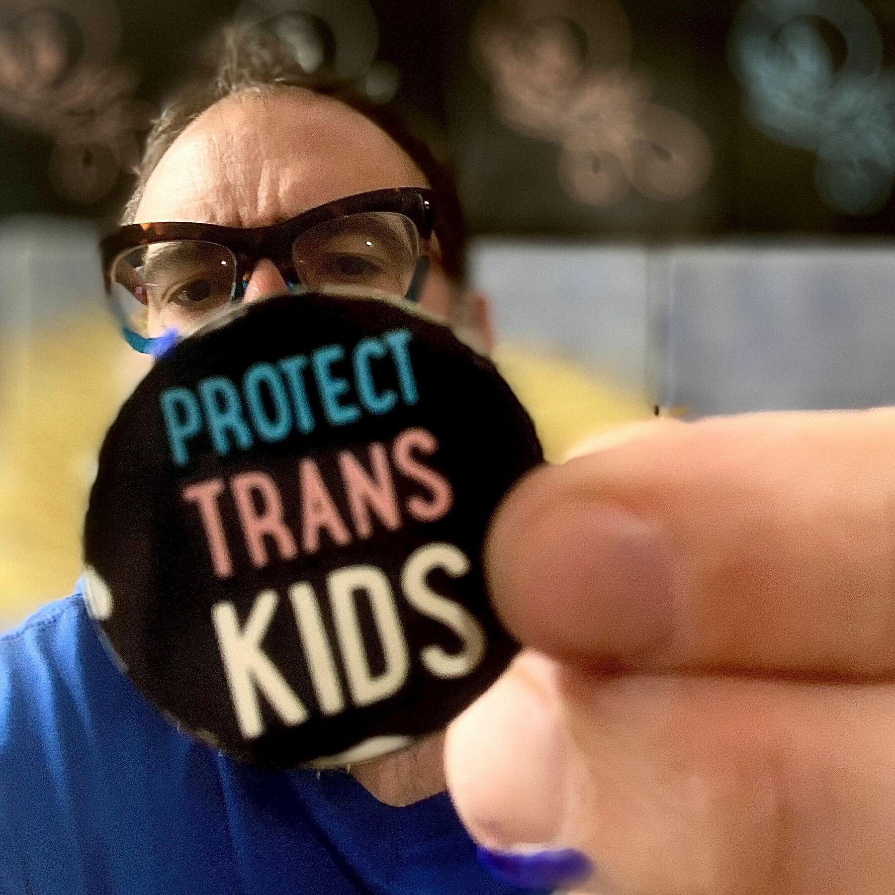 Mike Monteiro wearing glasses holding protect trans kids button.