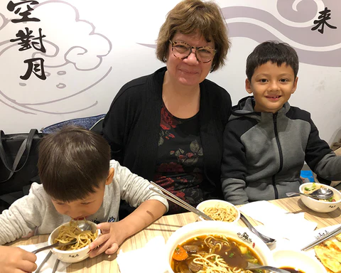 A white woman sitting next to two Taiwanese children eating at a table.