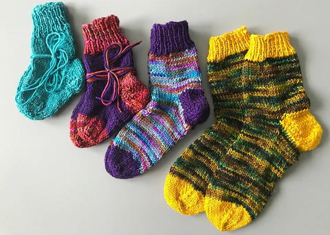 Four pairs of knitted socks. The yarn colors are blue, pink and purple, multicolored, and yellow.