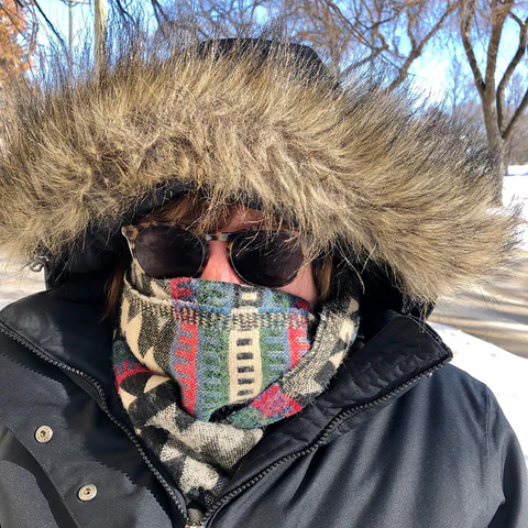 A woman wearing a big hooded coat, sunglasses, and a scarf covering her face.